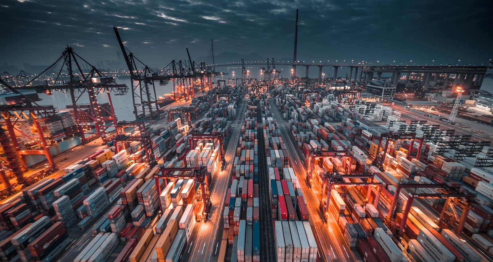 Container terminal at dusk with stacked shipping containers and gantry cranes