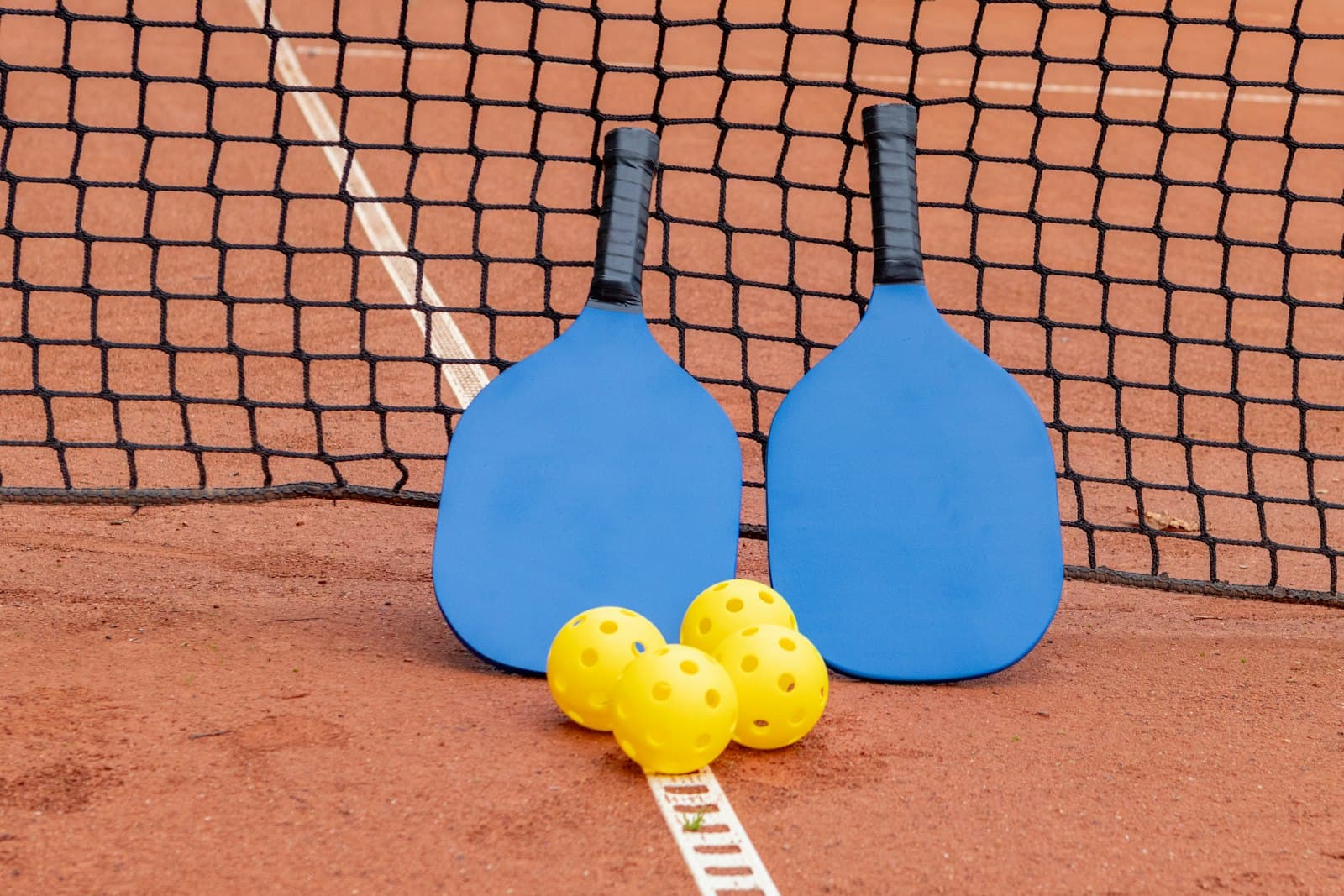 Two pickleball paddles leaning against a court net with three yellow balls